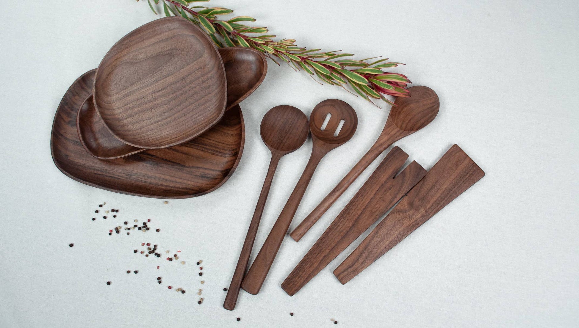 USA Wooden utensils including plates, spoons, and knives on a white surface with a sprig of rosemary.