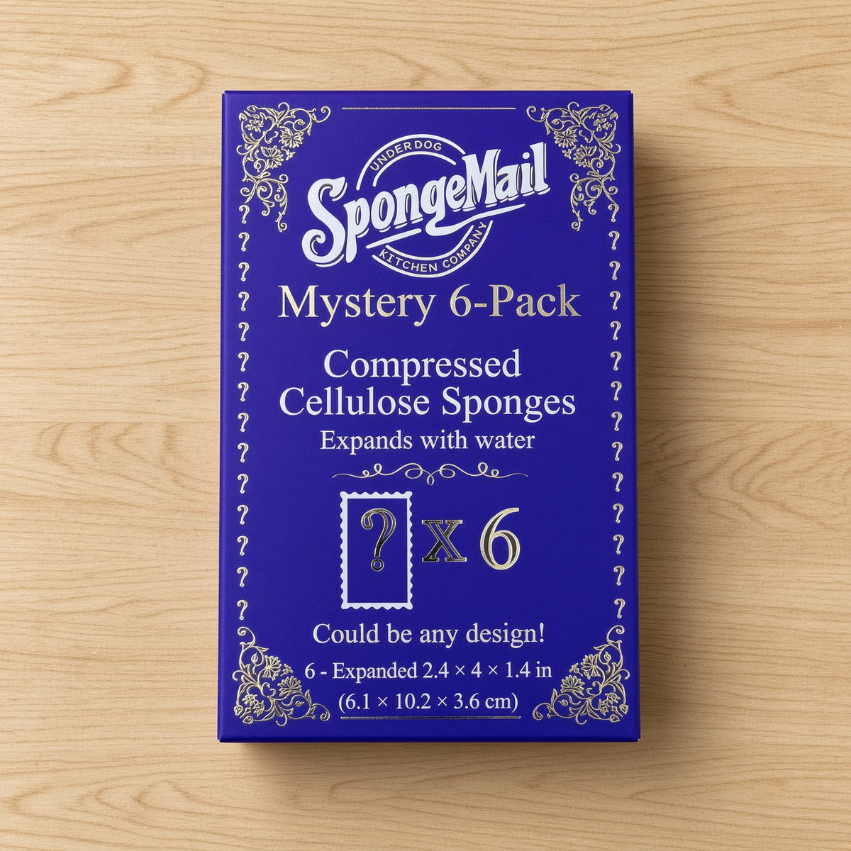 A blue rectangular box labeled 'SpongeMail Mystery 6-Pack' with white decorative text and ornamental borders, placed on a light wood surface.